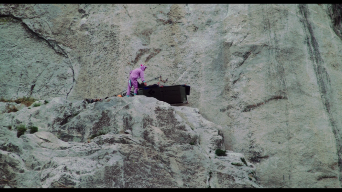 Screencap from the documentary "Free Solo," in which a climber in a unicorn onesie is visible on the face of "El Capitan" mountain in Yosemite.